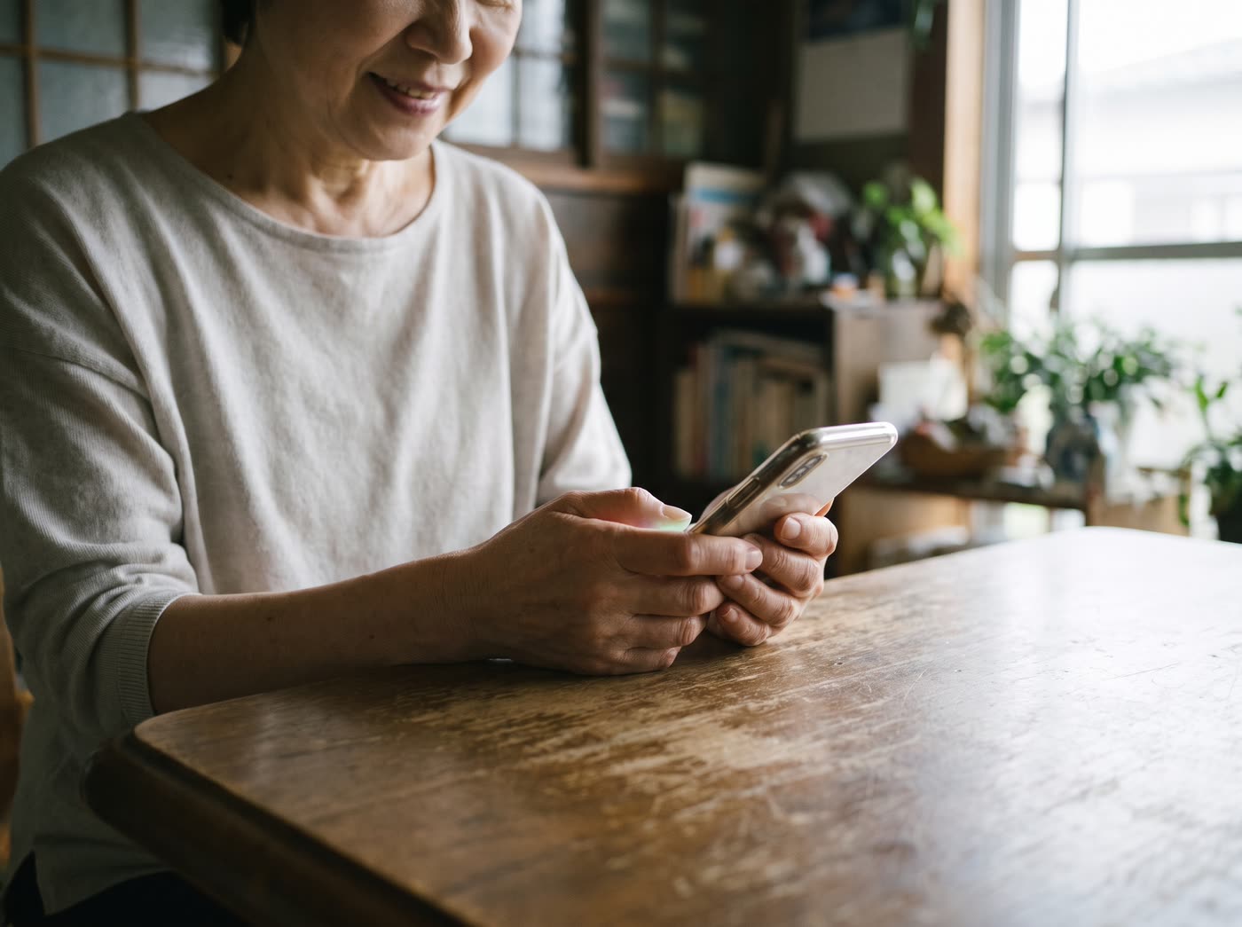 住宅のダイニングテーブルで、両手でスマートフォンを持って画面を見ている女性の手元